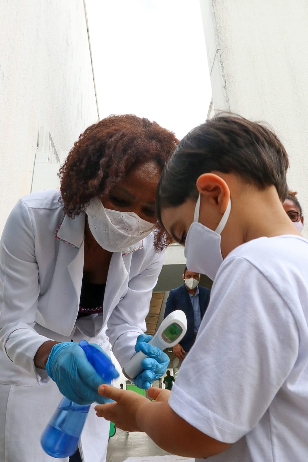 Professora higieniza mãos de aluno com álcool em gel