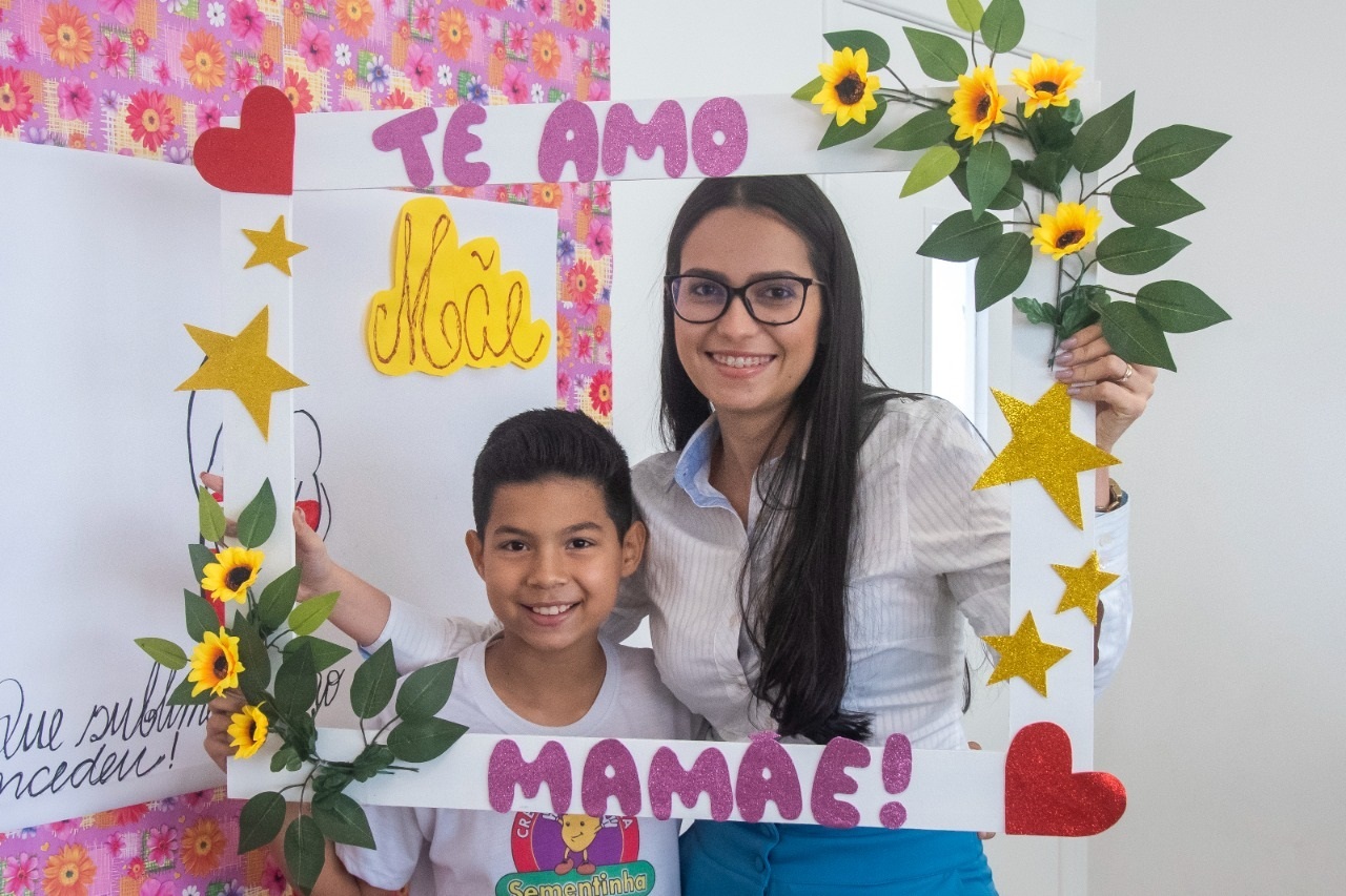 Mãe e filho posam na moldura de flores e coração criada especificamente para o momento  