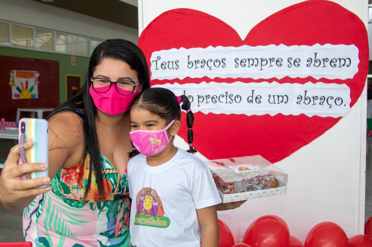 Mãe e filha registram o momento em frente ao cartaz com mensagem revelando a importância do abraço materno